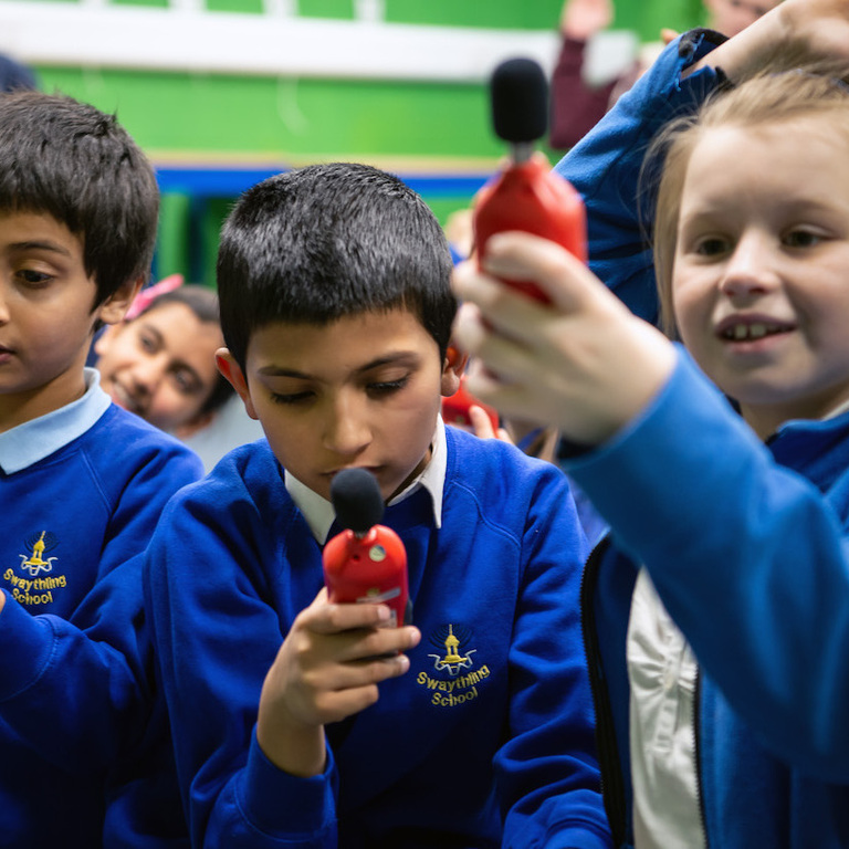 Three school children measuring noise levels using sound readers