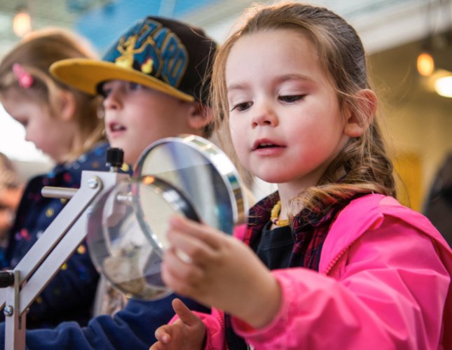 A young girl studies a scientific sample through a magnifying glass