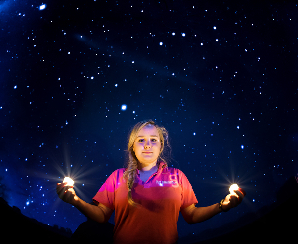 Planetarium photo showing a presenter in a Winchester Science Centre polo shirt holding a ball of light in each hand, against a backdrop of a starry night sky