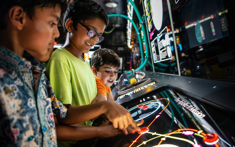 Interactive science exhibition photo showing three boys smiling and pressing buttons on an exhibit about space