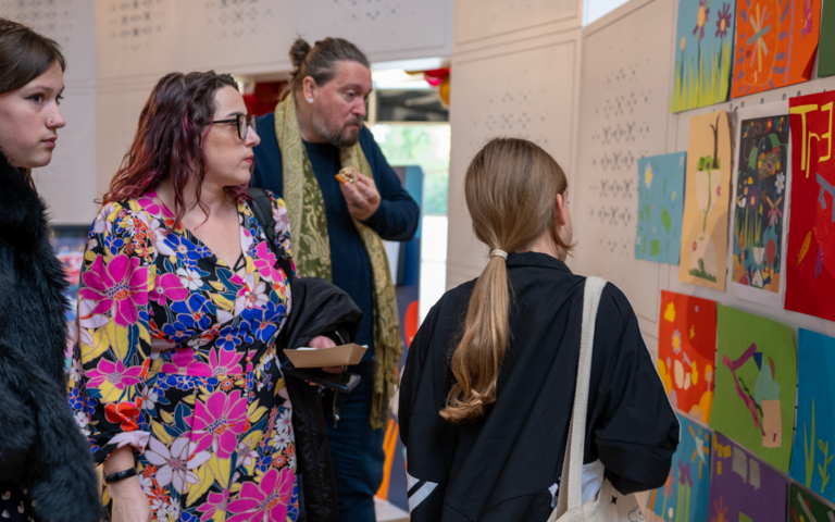A family are looking at a selection of artwork displayed on a white wall.