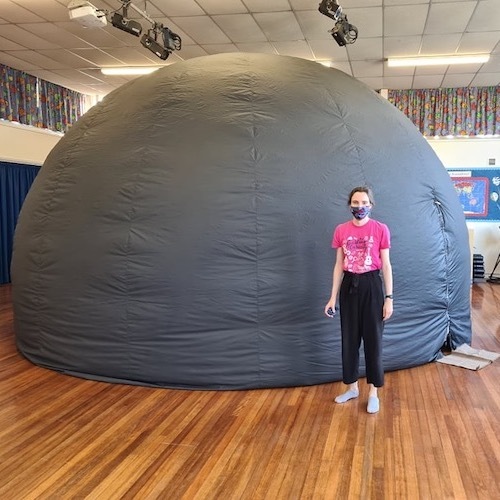 A presenter in a Winchester Science Centre polo shirt standing in front of the inflated mobile planetarium in a school hall