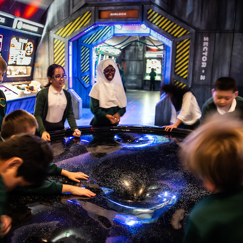 Interactive science exhibition photo showing a group of school children in a circle around a space-related exhibit as part of their school trip