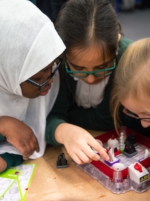 Three school children leaning over a table interacting with an activity as part of a workshop