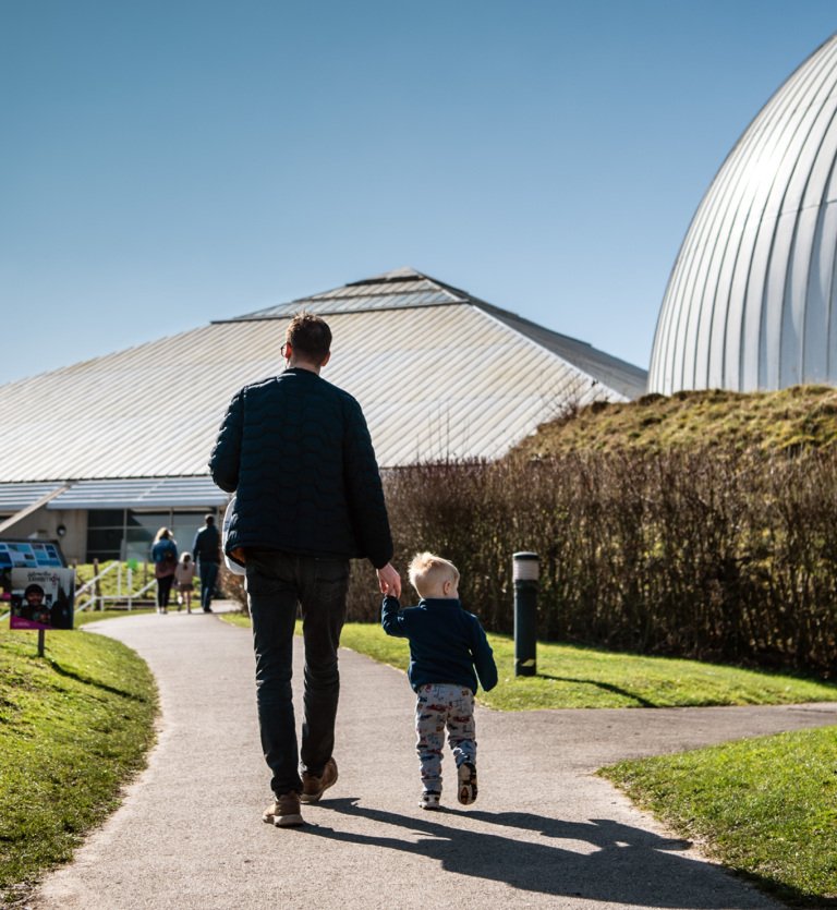 A man and a child are holding hands walking into Winchester Science Centre.