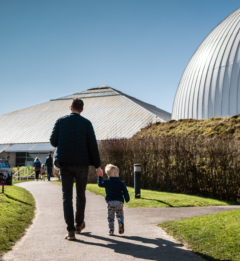 A man and a child are holding hands walking into Winchester Science Centre.