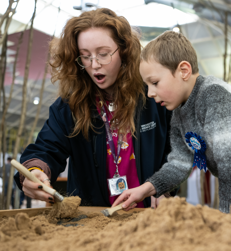 A science Inspirer and a little boy are digging for fossils together.